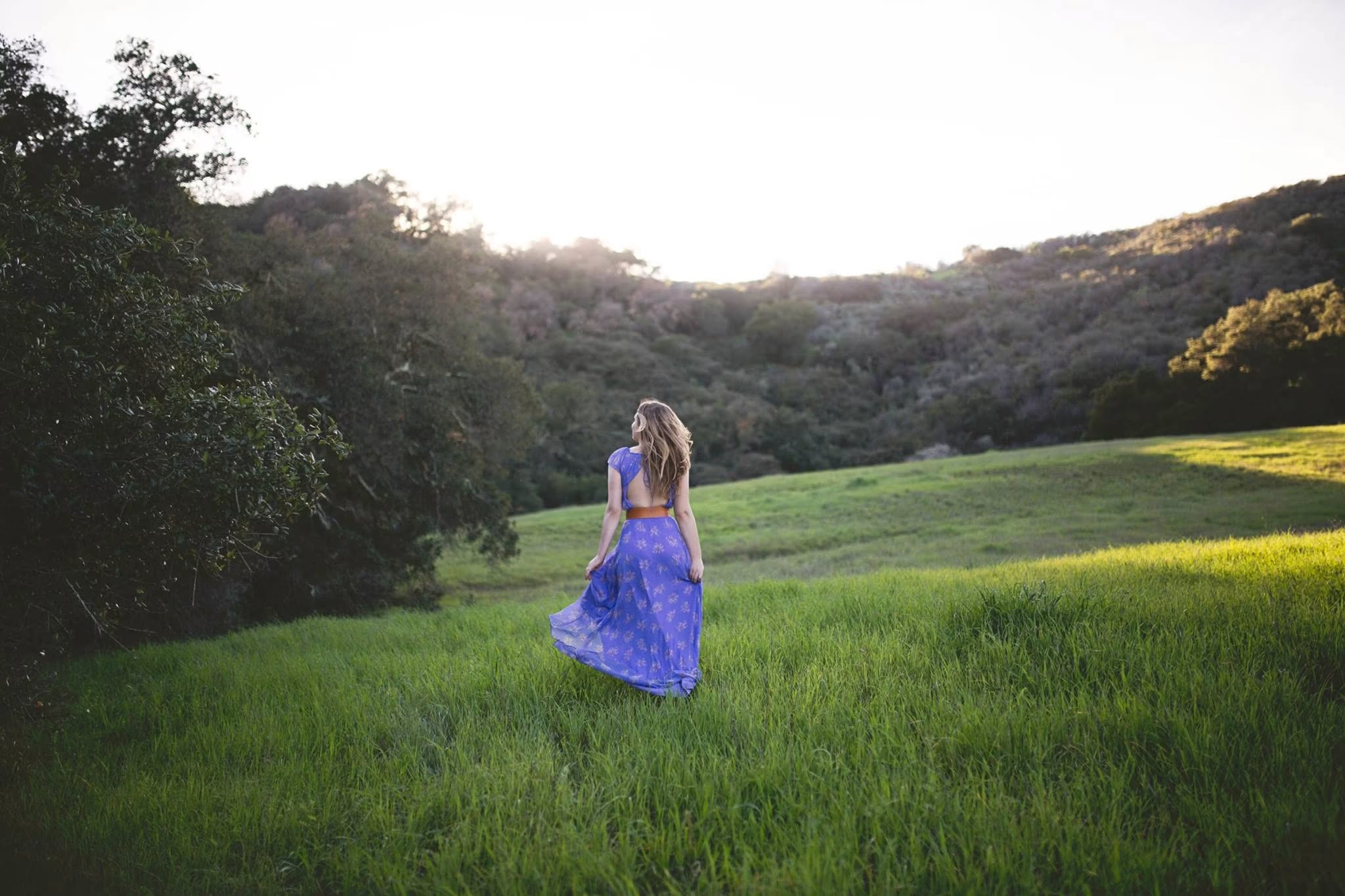 Dr. Michele Burklund in a violet dress, walking through a sunlit green meadow